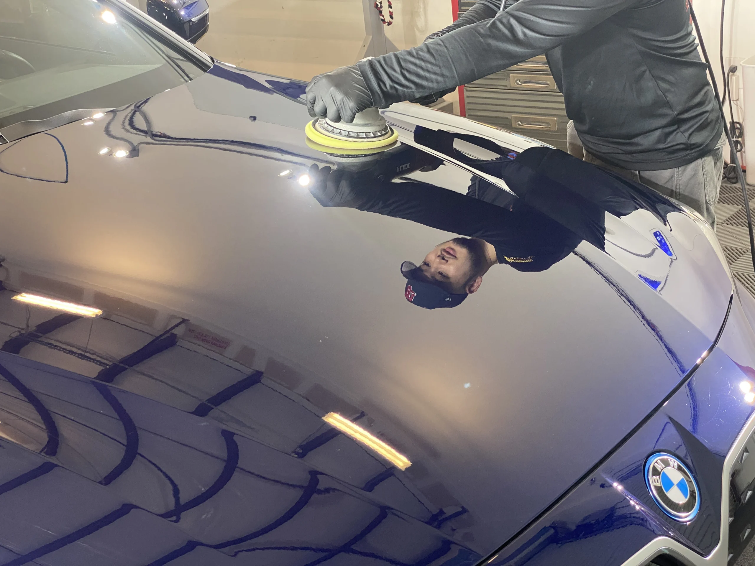 Reflection of a detailer at Phoenix Detailing in Melbourne FL polishing a hood of a car.